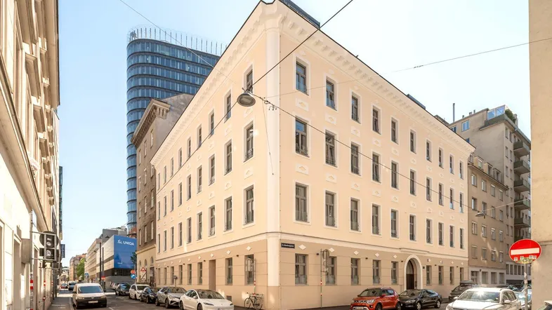 Historisches Eckgebäude in urbaner Umgebung mit moderner Architektur im Hintergrund.