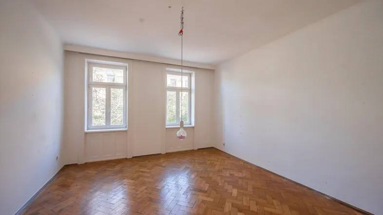 Helles Zimmer mit Fischgrätparkettboden und zwei großen Fenstern, bereit zur individuellen Gestaltung.