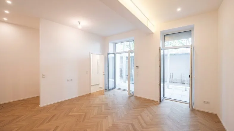 Helles Wohnzimmer mit Fischgrätparkett und großen Fenstertüren, die zu einem Balkon führen.