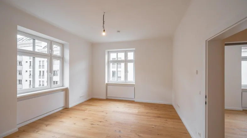Helles Zimmer mit Holzboden und zwei Fenstern, bereit zur individuellen Gestaltung.