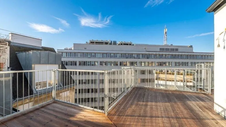 Große Dachterrasse mit Holzboden und Metallgeländer, bietet weiten Blick über die Stadt.