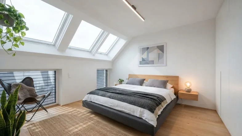 Helles Schlafzimmer im Dachgeschoss mit Holzboden, Dachfenstern und moderner Einrichtung.