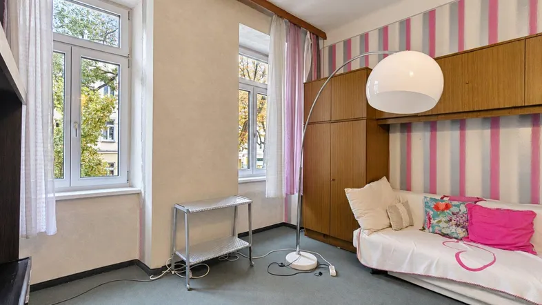 Gemütliches Zimmer mit gestreifter Tapete, Schrankwand und Blick ins Grüne durch die Fenster.