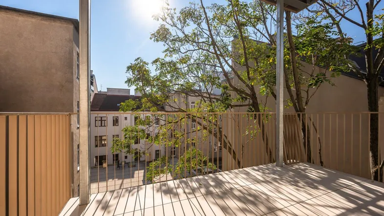 Heller Balkon mit modernem Geländer und Blick auf den begrünten Innenhof.