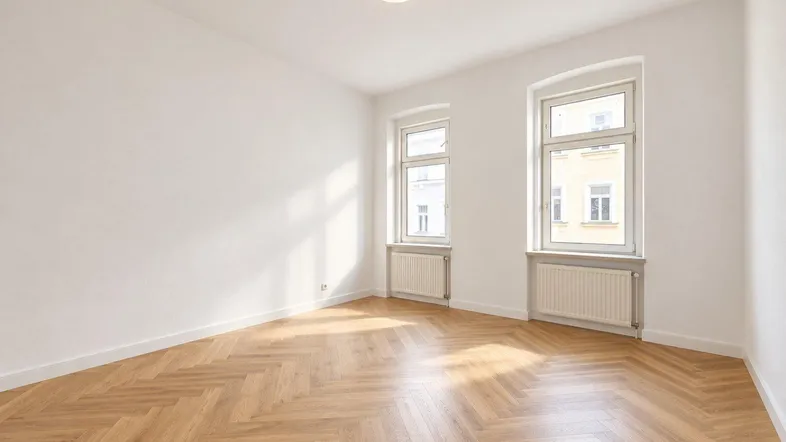 Helles, leeres Zimmer mit Fischgrätparkett und zwei Fenstern, die viel Tageslicht hereinlassen.
