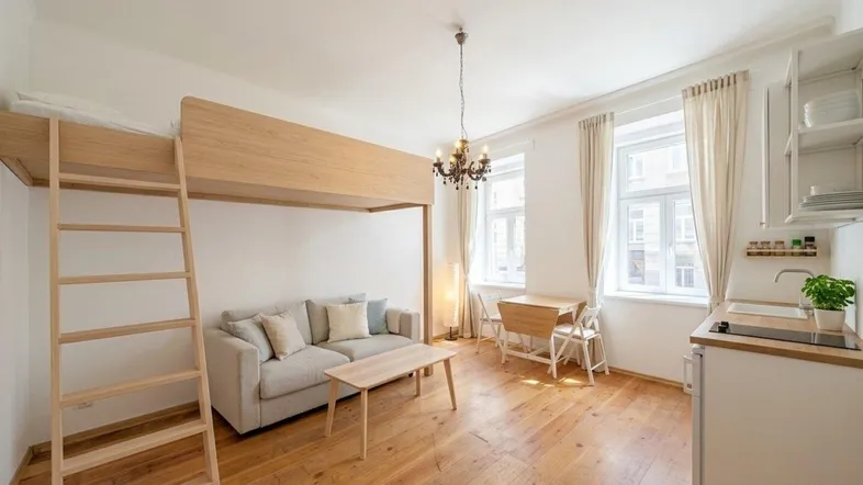 Heller Wohnraum mit Hochbett, Sofa, Esstisch und kleiner Küchenzeile, ideal für ein Studio-Apartment.