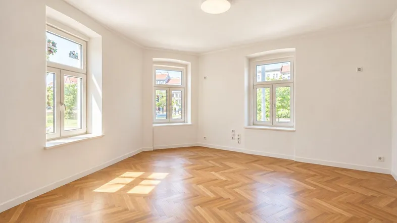 Helles Zimmer mit Fischgrätparkett und mehreren Fenstern, ideal für Wohn- oder Schlafbereich.