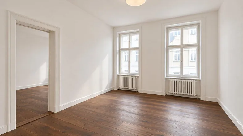 Helles, frisch renoviertes Zimmer mit dunklem Parkettboden und zwei großen Fenstern.