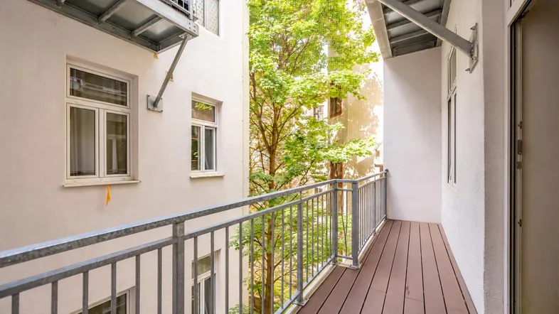 Heller Balkon mit Holzboden und Metallgeländer, bietet einen ruhigen Blick in den begrünten Innenhof.