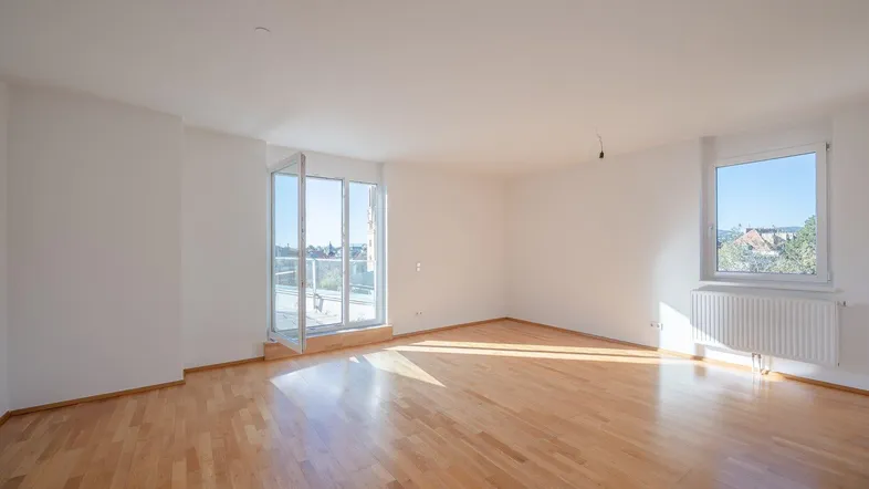 Helles, leeres Wohnzimmer mit Parkettboden und Zugang zu einer Terrasse.