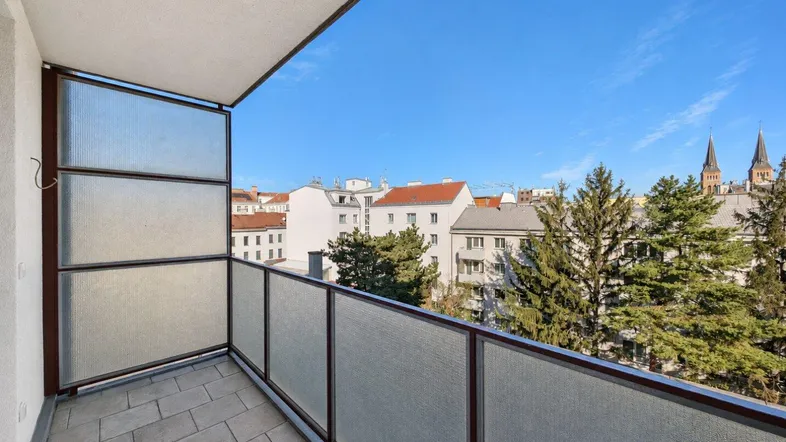 Balkon mit Fliesenboden und Blick über die Stadt mit grünen Bäumen und Kirchtürmen.