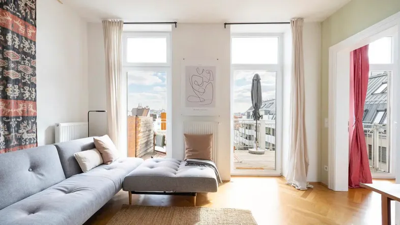 Helles Wohnzimmer mit Parkettboden, modernem Sofa und Zugang zu einem sonnigen Balkon mit Stadtblick.