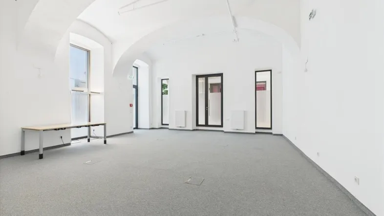Geräumiger, heller Büroraum mit gewölbten Decken, großen Fenstern und grauem Teppichboden.