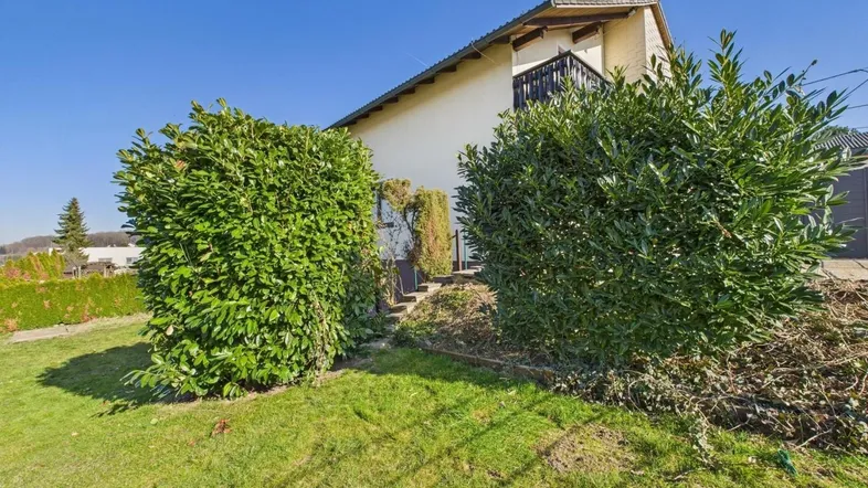 Seitenansicht des Hauses mit gepflegtem Rasen, großen Büschen und einem kleinen Balkon.