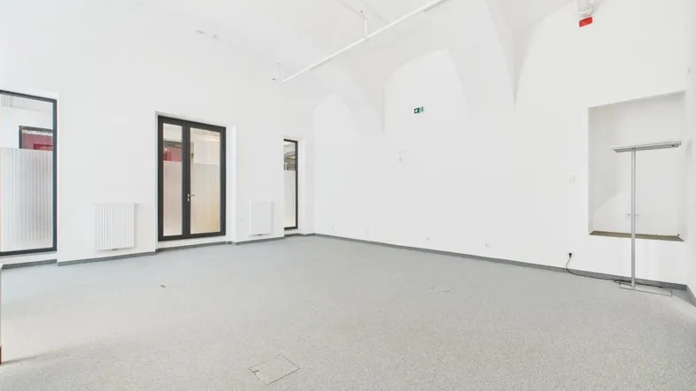 Geräumiger, heller Büroraum mit hohen Gewölbedecken und grauem Teppichboden, bereit zur individuellen Gestaltung.