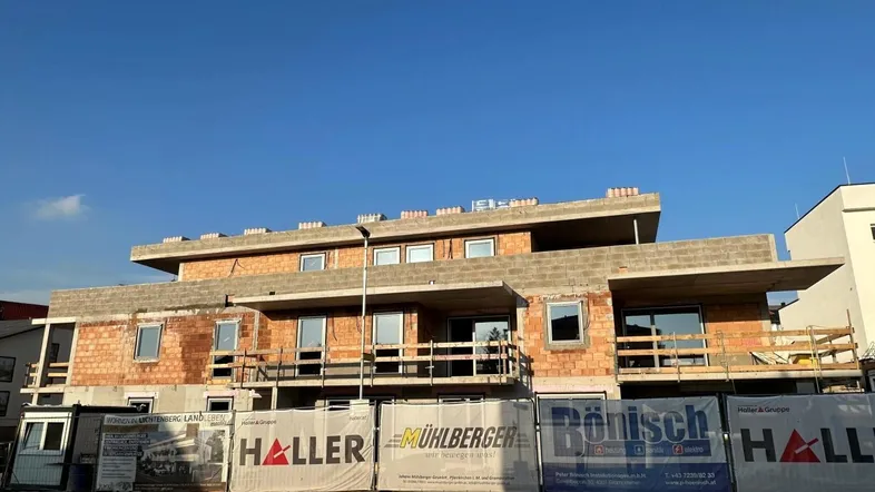 Rohbau eines modernen Wohngebäudes mit sichtbaren Ziegelwänden und Betonelementen unter klarem Himmel.