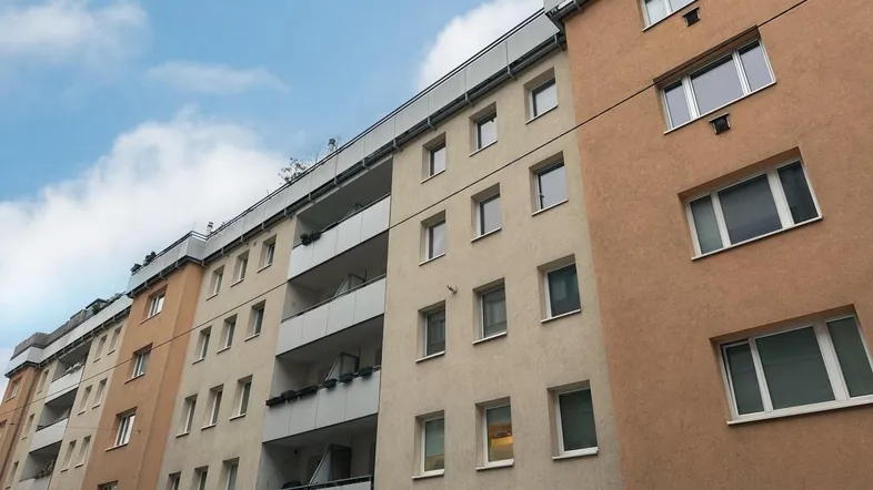 Fassade eines Mehrfamilienhauses mit mehreren Balkonen und Fenstern unter blauem Himmel.