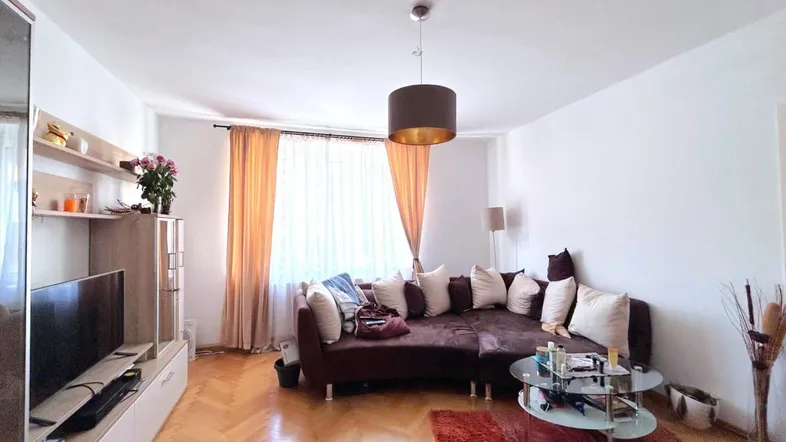 Helles Wohnzimmer mit bequemer Eckcouch, Parkettboden und Blick nach draußen durch große Fenster.