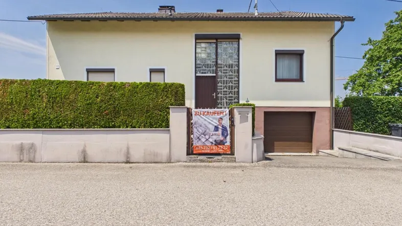 Vorderansicht des Hauses mit gepflegter Hecke und Garagenzufahrt unter blauem Himmel.