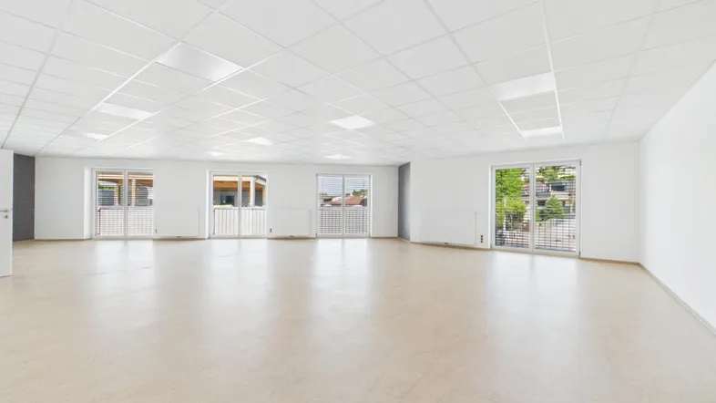 Großer, heller Raum mit vielen Fenstern, hellem Boden und Rasterdecke, ideal für gewerbliche Nutzung.