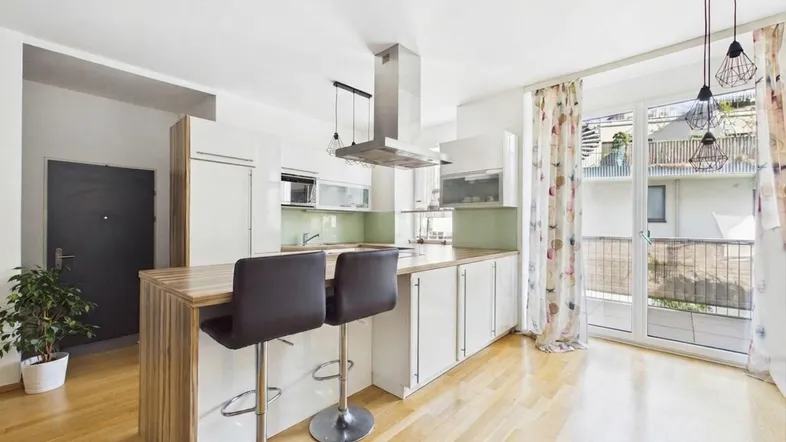 Helle offene Küche mit Holzboden, Kücheninsel und Zugang zum Balkon.