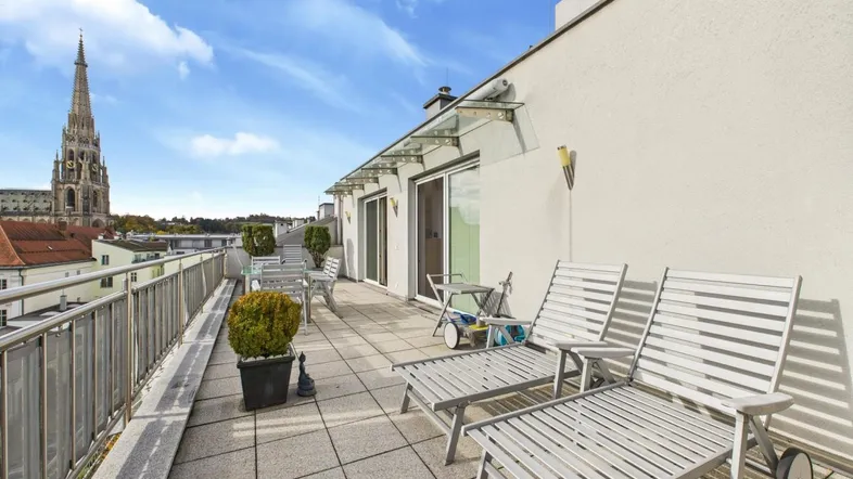 Große Dachterrasse mit Liegestühlen und weitem Blick auf die Stadt und Kirchturm.
