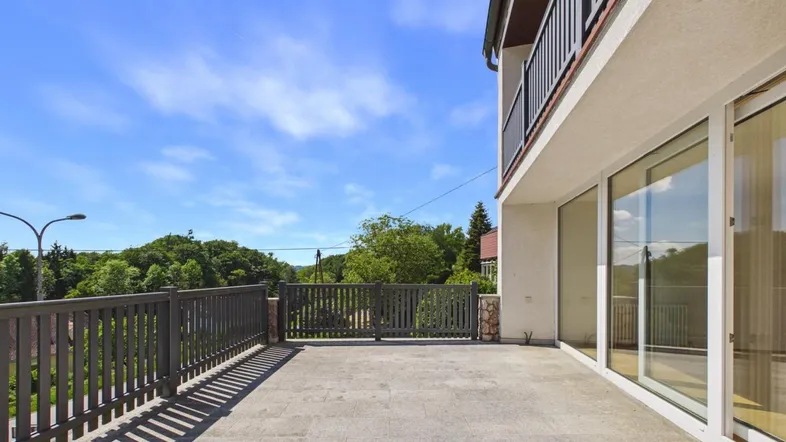 Große, gepflasterte Terrasse mit Blick ins Grüne und moderner Balustrade unter blauem Himmel.