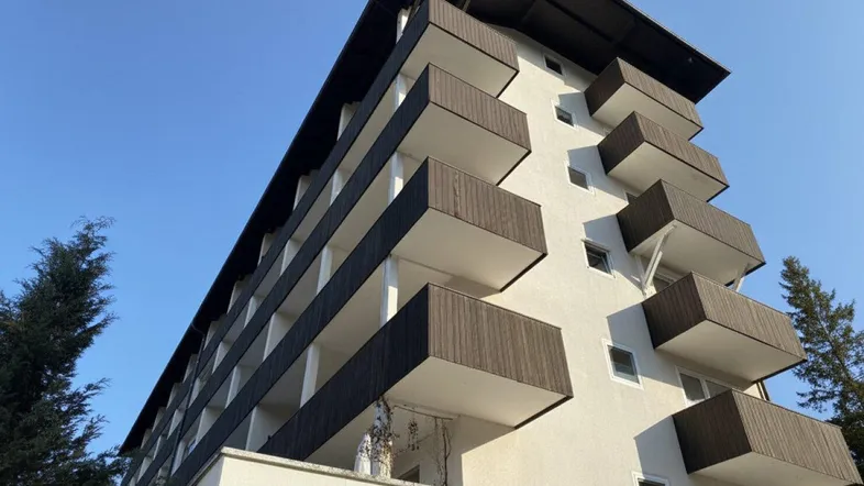 Mehrstöckiges Wohngebäude mit zahlreichen Balkonen und dunklen Holzbalkonverkleidungen unter blauem Himmel.