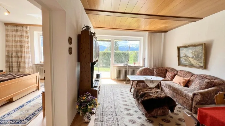 Gemütliches Wohnzimmer mit Holzdecke, traditionellen Möbeln und weitem Blick ins Grüne.