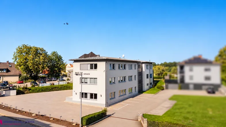 Luftaufnahme eines modernen Bürogebäudes mit großem Parkplatz unter klarem blauem Himmel.
