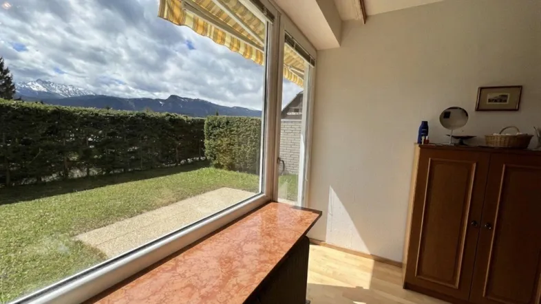 Heller Wohnraum mit großen Fenstern, die einen weiten Blick auf die Berge und den grünen Garten bieten.