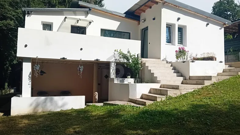 Modernes weißes Haus mit gestuften Terrassen und Treppen, umgeben von viel Grün und Bäumen.