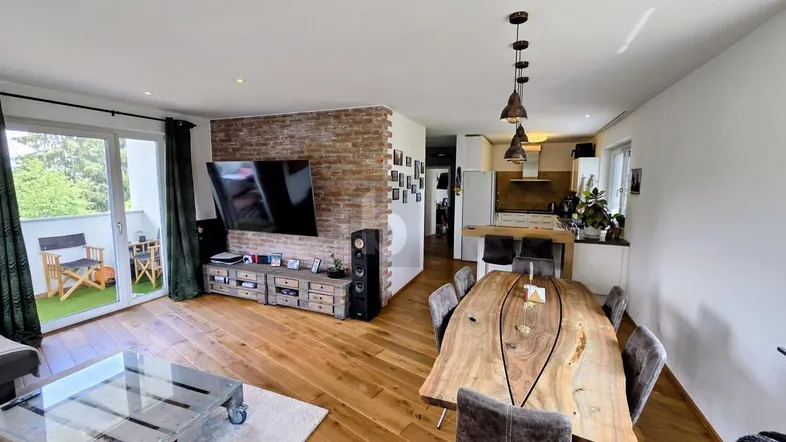 Heller offener Wohn-Essbereich mit Holzboden, Ziegelwand und Zugang zu einem Balkon.