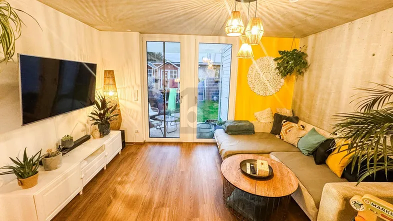 Helles Wohnzimmer mit Holzboden, gemütlichem Sofa und Zugang zu einer Terrasse oder Garten.