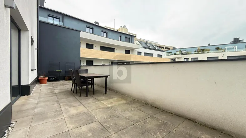 Geräumige Terrasse mit Fliesenboden und Essbereich im Freien, umgeben von modernen Gebäuden.