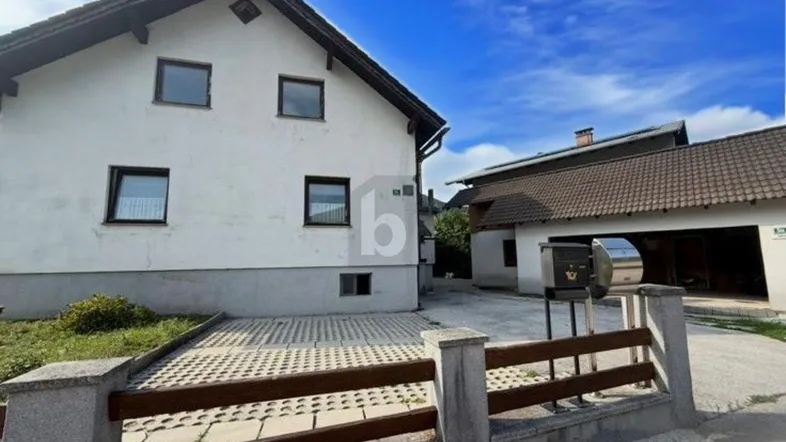 Außenansicht eines weißen Einfamilienhauses mit gepflasterter Auffahrt und Zaun unter blauem Himmel.