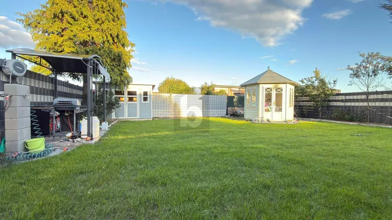 Großer grüner Garten mit Rasenfläche, einem Gartenhaus und einem überdachten Grillbereich.