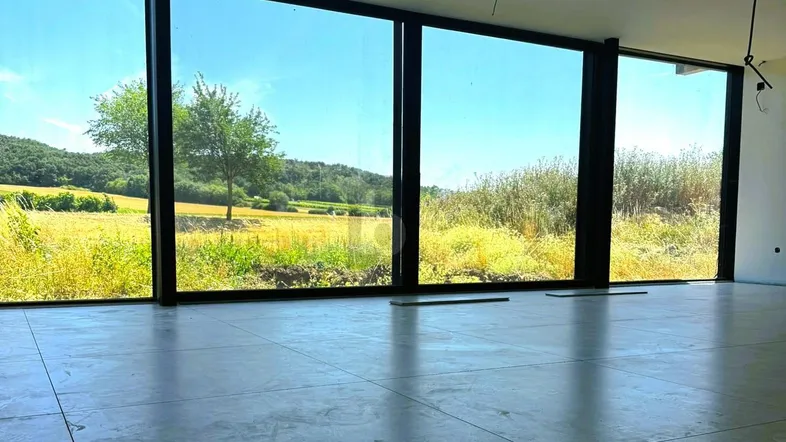 Heller Raum mit großen Fenstern und weitem Blick auf die grüne Landschaft, ausgestattet mit Fliesenboden.