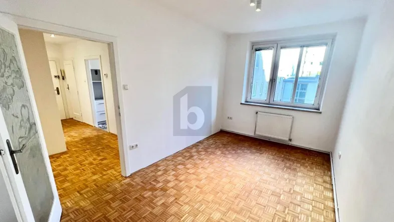 Helles Zimmer mit Parkettboden und Fenster, das viel Tageslicht hereinlässt.