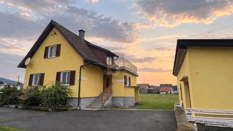 Gelbes Einfamilienhaus mit Satteldach und separatem Nebengebäude bei Sonnenuntergang.