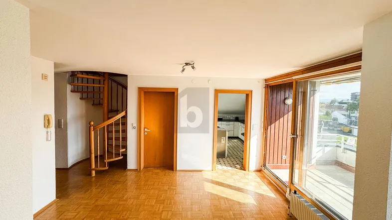 Heller Wohnbereich mit Parkettboden, Wendeltreppe und Zugang zum Balkon sowie zur Küche.