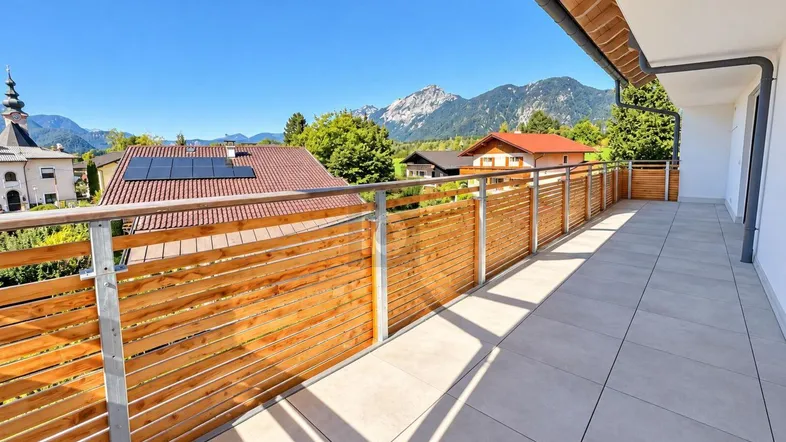 Großer Balkon mit Holzelementen, Fliesenboden und weitem Bergblick unter blauem Himmel.