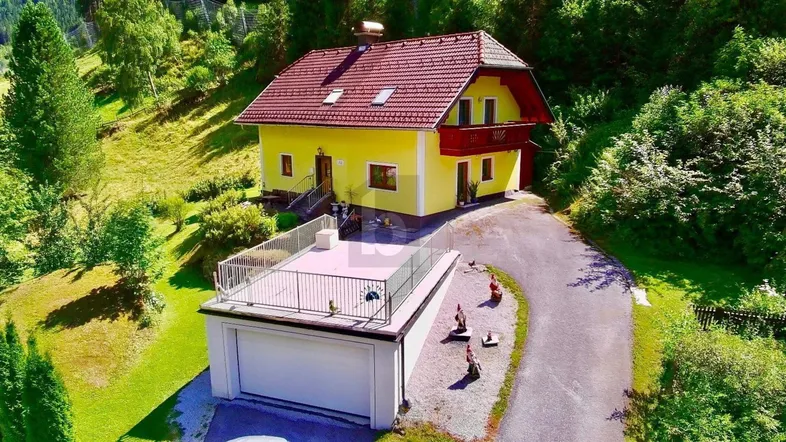 Gelbes Haus mit rotem Dach, Garage und Dachterrasse in grüner Berglandschaft.
