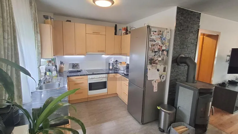 Moderne Küche mit hellen Holzschränken, integrierten Geräten und einem Holzofen im offenen Bereich.