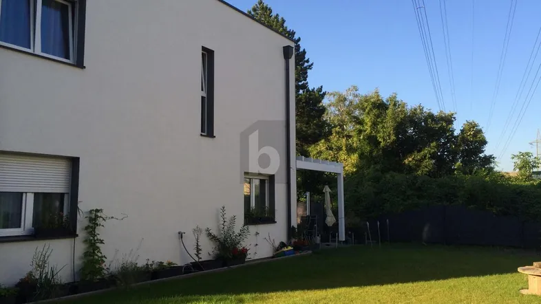 Moderne Hausfassade mit weißem Putz, großem grünen Garten und einer überdachten Terrasse.
