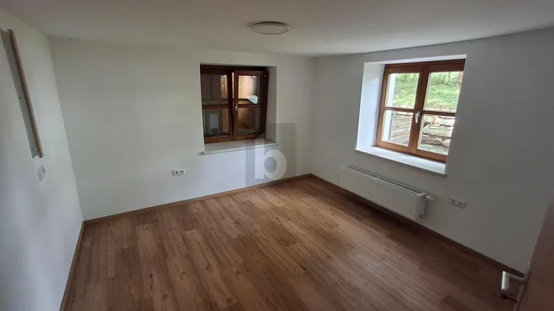 Helles Zimmer mit Holzboden und zwei Fenstern, bereit zur individuellen Gestaltung.