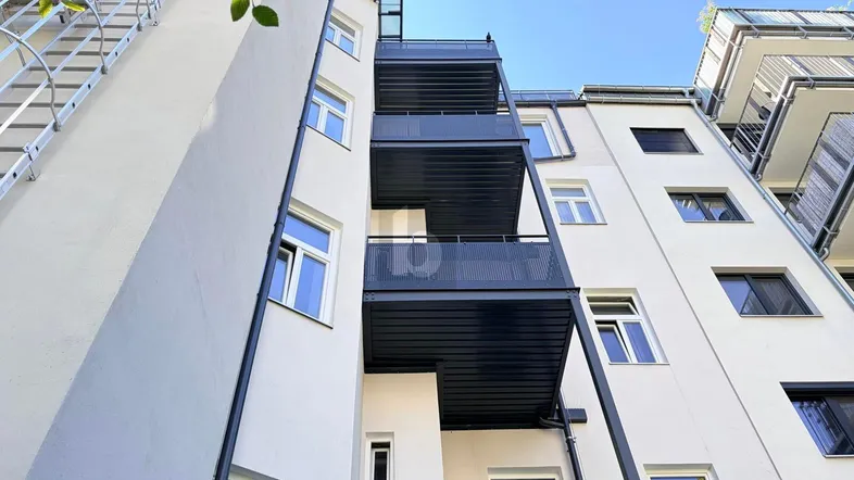 Moderne Gebäudefassade mit mehreren Balkonen und großen Fenstern, die viel Licht hereinlassen.