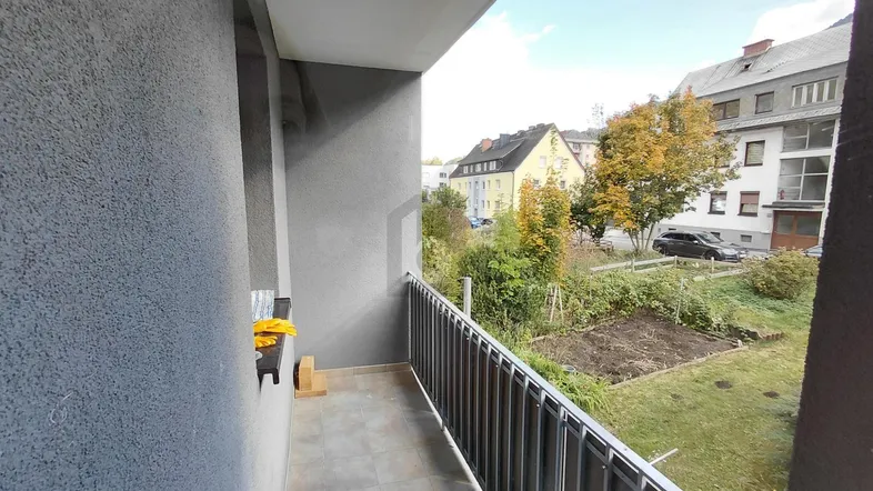 Balkon mit Fliesenboden und Blick auf den Garten sowie umliegende Gebäude.