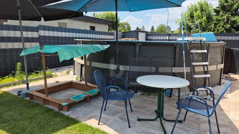 Gartenbereich mit großem Aufstellpool, Sandkasten und Sitzgelegenheiten unter Sonnenschirmen.