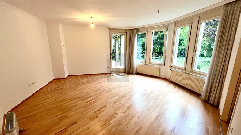 Helles Wohnzimmer mit Parkettboden und großen Fenstern, die viel Tageslicht hereinlassen und Zugang zum Garten bieten.